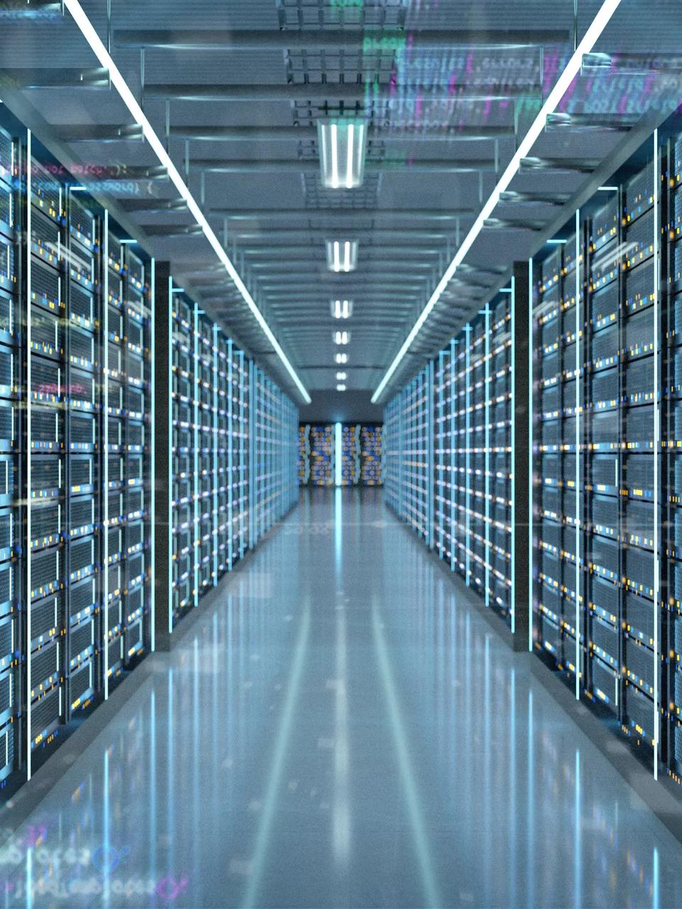 A long, symmetrical perspective view down an aisle in a massive data center server room. The walls are lined with tall, dark server racks, illuminated by vertical strips of cool blue light.