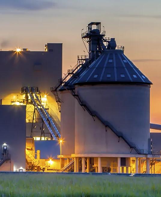View of a tall silo and processing towers silhouetted during sunset.