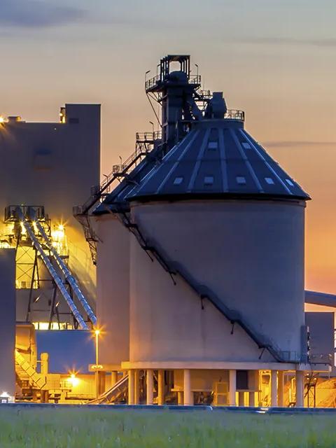 View of a tall silo and processing towers silhouetted during sunset.