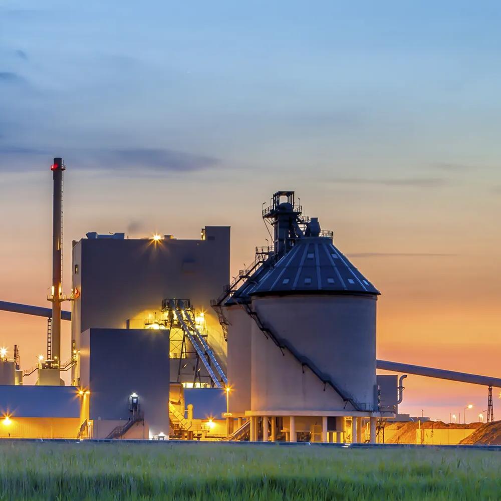 View of a tall silo and processing towers silhouetted during sunset.