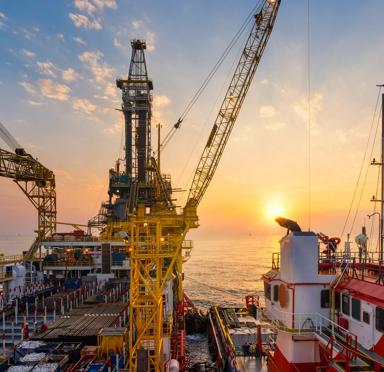 Offshore oil drilling rig operation platform in oil and gas industry with supply boat to transfer chemical during sunrise. Industry concept.