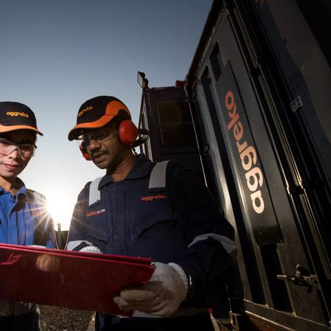 2 people looking at a clipboard alongside an aggreko generator