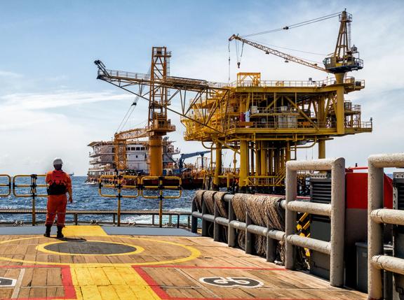 Worker on the boat look at Oil and gas industrial platform in the gulf or the sea, The world energy of oil and gas company, Offshore oil and rig construction. Industry concept.