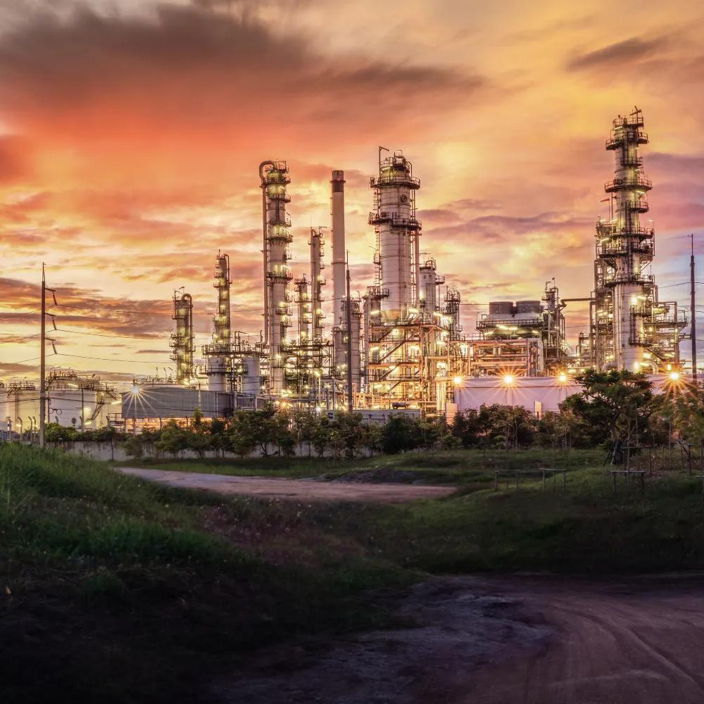 View of a petrochemical plant at the end of a dirt road against a cloudy sunset sky