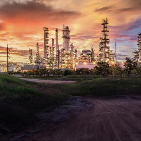 View of a petrochemical plant at the end of a dirt road against a cloudy sunset sky