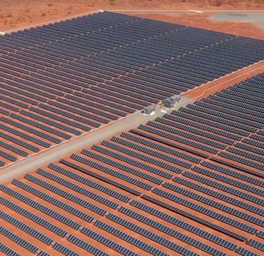 Aerial view of a large solar farm featuring rows of solar panels set on red desert terrain.