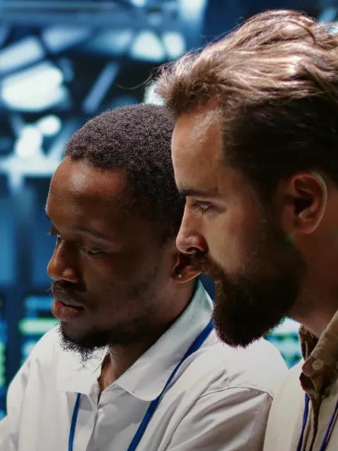 Two technicians in a data center aisle, looking at a tablet together while standing in front of rows of servers