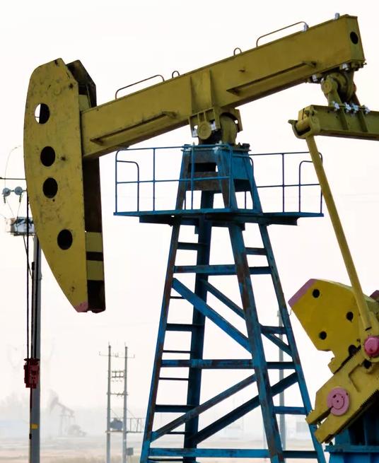 A hazy, distant view of a field containing several yellow and black oil pump jacks operating in a flat, open landscape.