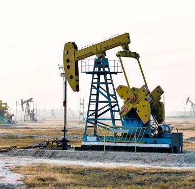 A yellow oil rig in a field with multiple oil rigs in the background and mist on the horizon