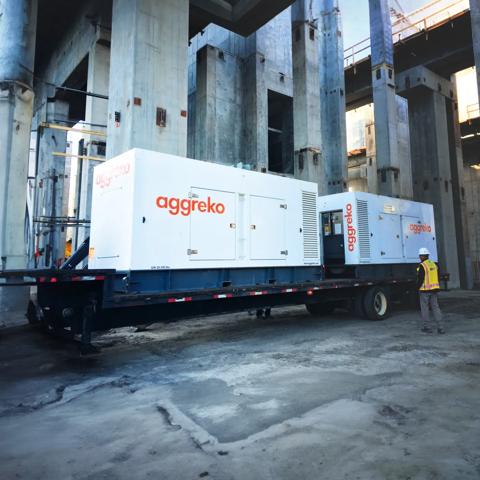 Deux générateurs Aggreko blancs montés sur remorque sur un chantier et un ouvrier à côté de l’équipement