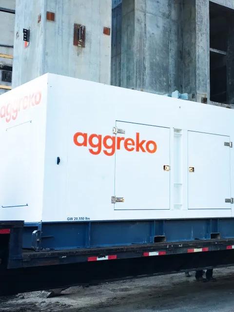 Two trailer-mounted white Aggreko generators at a worksite and a worker next to the equipment