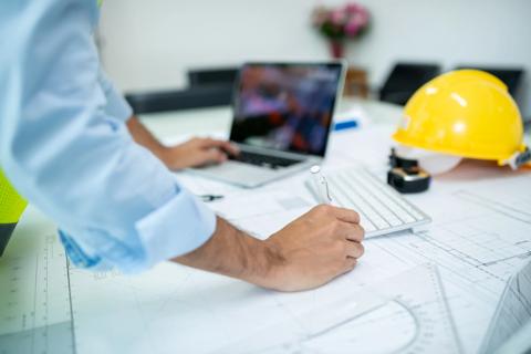 A site engineer leans over construction plans on a drafting table.