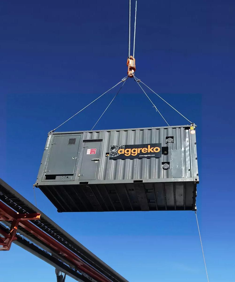A black Aggreko generator being lifted on a worksite against a blue sky