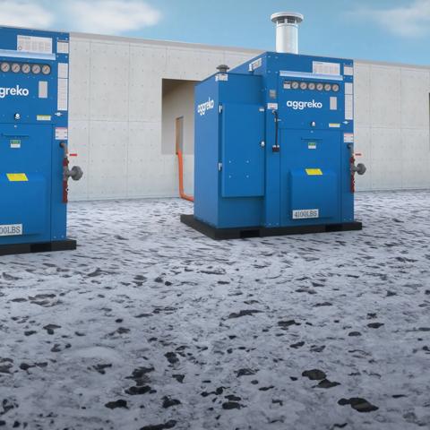 Two large, blue Aggreko industrial modular units featuring control panels with multiple circular gauges and piping connections, in front of a white concrete building.
