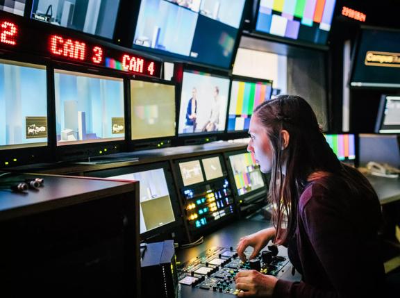 A university student looking at various screens while using tv studio equipment.