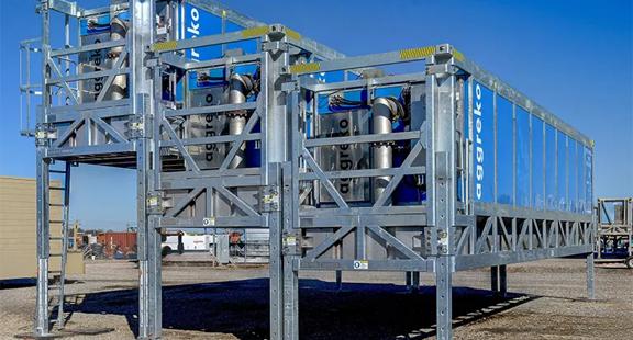 Two large, gray modular frames holding blue industrial Aggreko container units, set outdoors under a clear sky