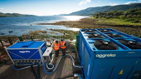Two workers near the sea between two blue pieces of Aggreko hvac equipment