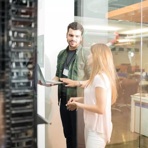 Two business people standing in server room with laptop and discussing