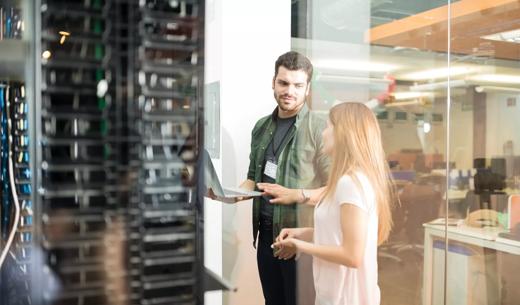 Two business people standing in server room with laptop and discussing