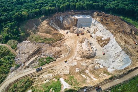 Aerial view of open pit mining site of limestone materials for construction industry with excavators and dump trucks.
