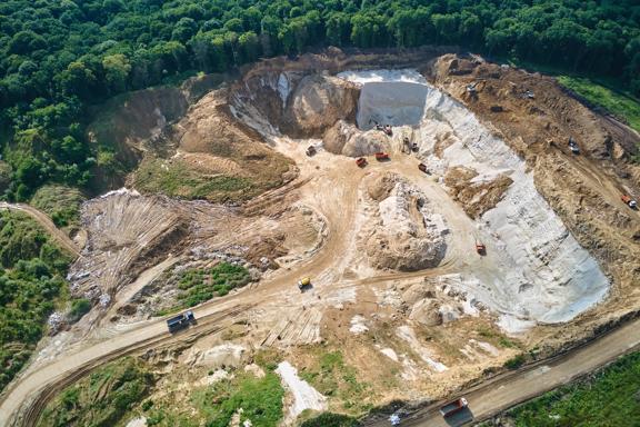 Aerial view of open pit mining site of limestone materials for construction industry with excavators and dump trucks.