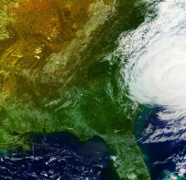 Satellite image showing a green landscape on the left and swirling clouds over the ocean on the right, depicting a storm.