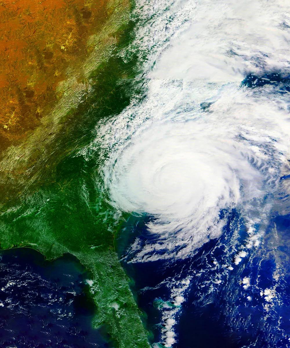 Satellite image showing a green landscape on the left and swirling clouds over the ocean on the right, depicting a storm.