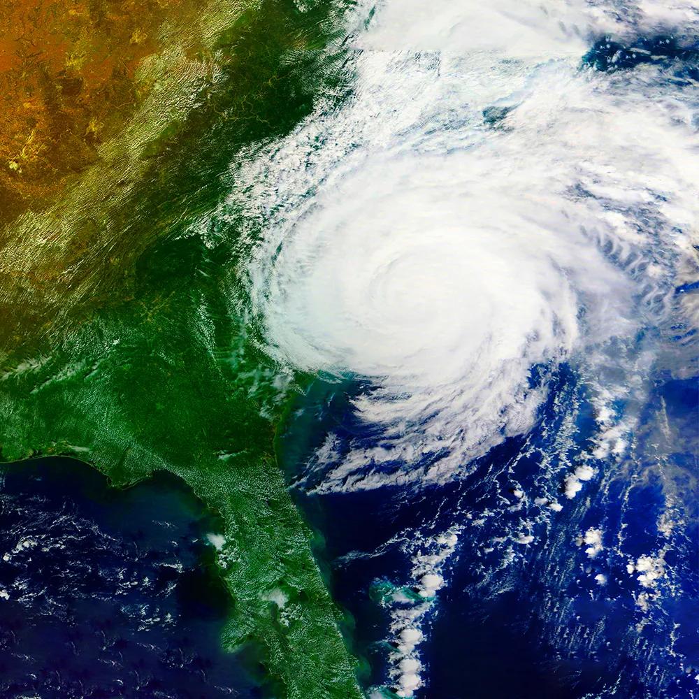 Satellite image showing a green landscape on the left and swirling clouds over the ocean on the right, depicting a storm.