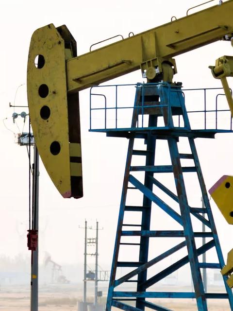 A yellow oil rig in a field with multiple oil rigs in the background and mist on the horizon