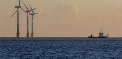 Offshore wind farm turbines on the horizon with passing ship. Green energy production and environmental conservation from sustainable resource. Beautiful tranquil image of massive turbines on the East coast of England.