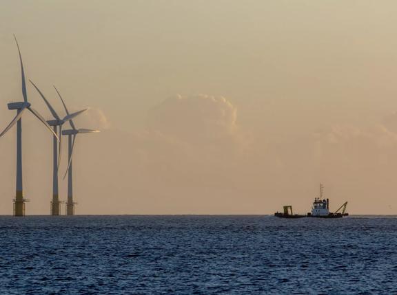 Offshore wind farm turbines on the horizon with passing ship. Green energy production and environmental conservation from sustainable resource. Beautiful tranquil image of massive turbines on the East coast of England.