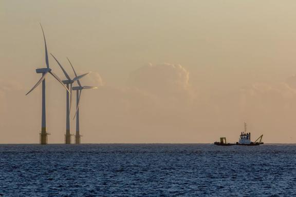 Offshore wind farm turbines on the horizon with passing ship. Green energy production and environmental conservation from sustainable resource. Beautiful tranquil image of massive turbines on the East coast of England.