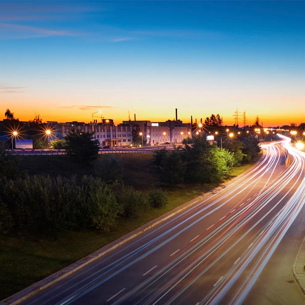 City road at sunset with multiple lights from speeding cars.