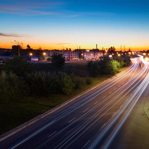 City road at sunset with multiple lights from speeding cars.
