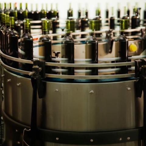 A close-up, dynamic shot of a conveyor belt line showing a grid of dark green bottles moving through a filling or processing station in a factory.