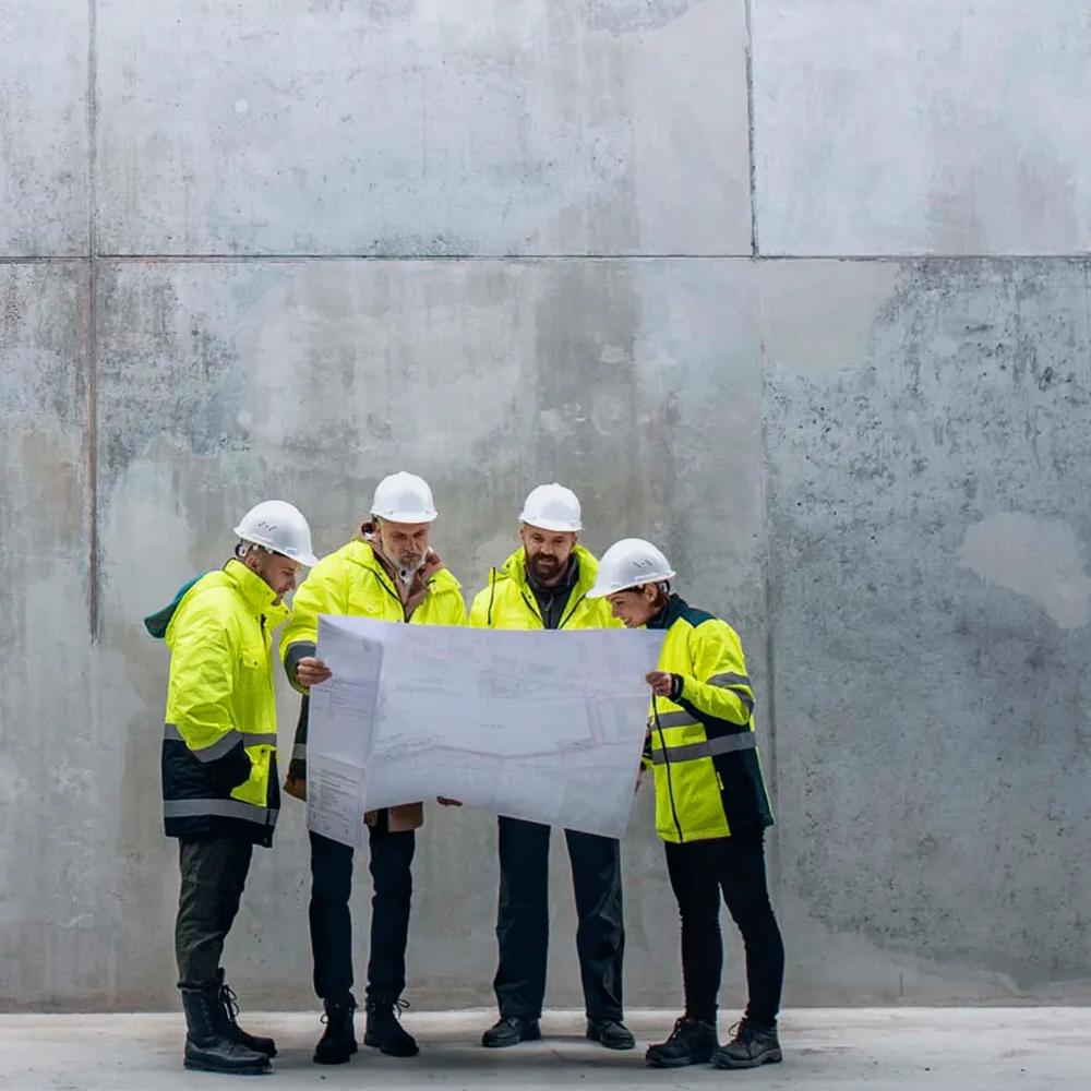 Group of construction contractors glances together at a plan in front of a large concrete building
