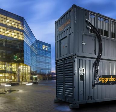 Aggreko has generators sitting outside a modern glass building at dusk, showcasing a blend of technology and architecture.