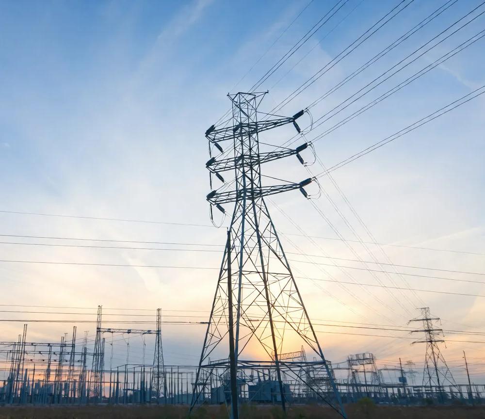 Power lines and tall transmission towers silhouetted against a colorful sunset sky.