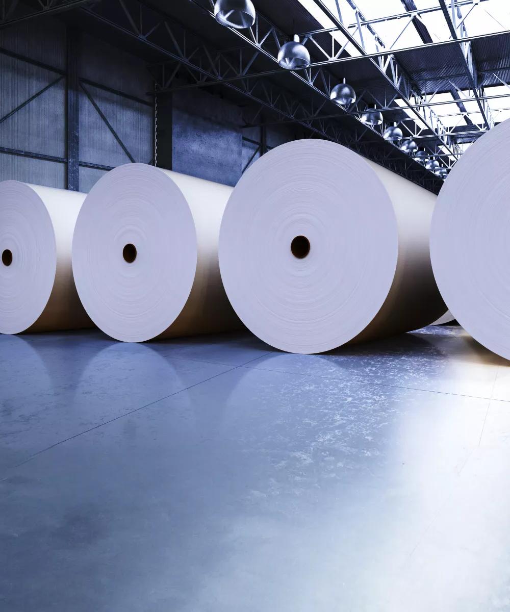 Quatre rouleaux de papier géants à l’intérieur d’une usine de papier gris