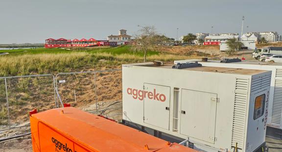 A white Aggrkeo generator with the orange logo at a worksite next to a grass field 