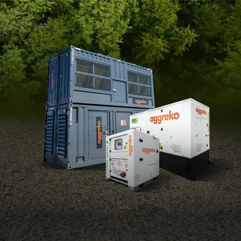 Three Aggreko power units, two white generators, and a large, stacked gray container unit, all on dirt in front of a forest.