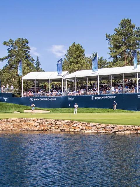 Golf players on a green field and a crowd watching from the stands at the BMW Championship Tournament