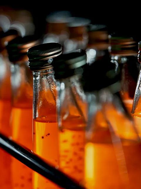 Close-up view of multiple bottles filled with an orange liquid, in a production line.