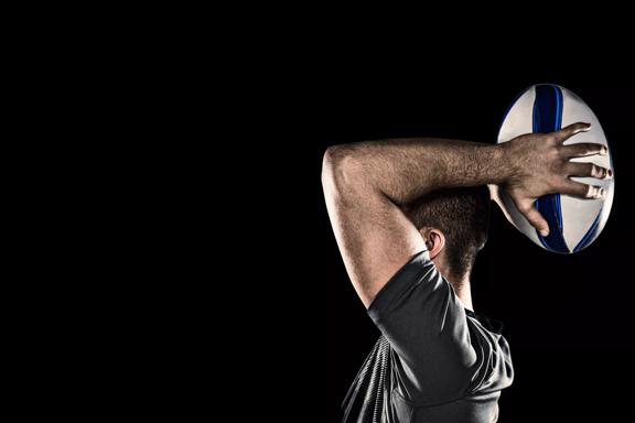 Rugby player throwing ball against black