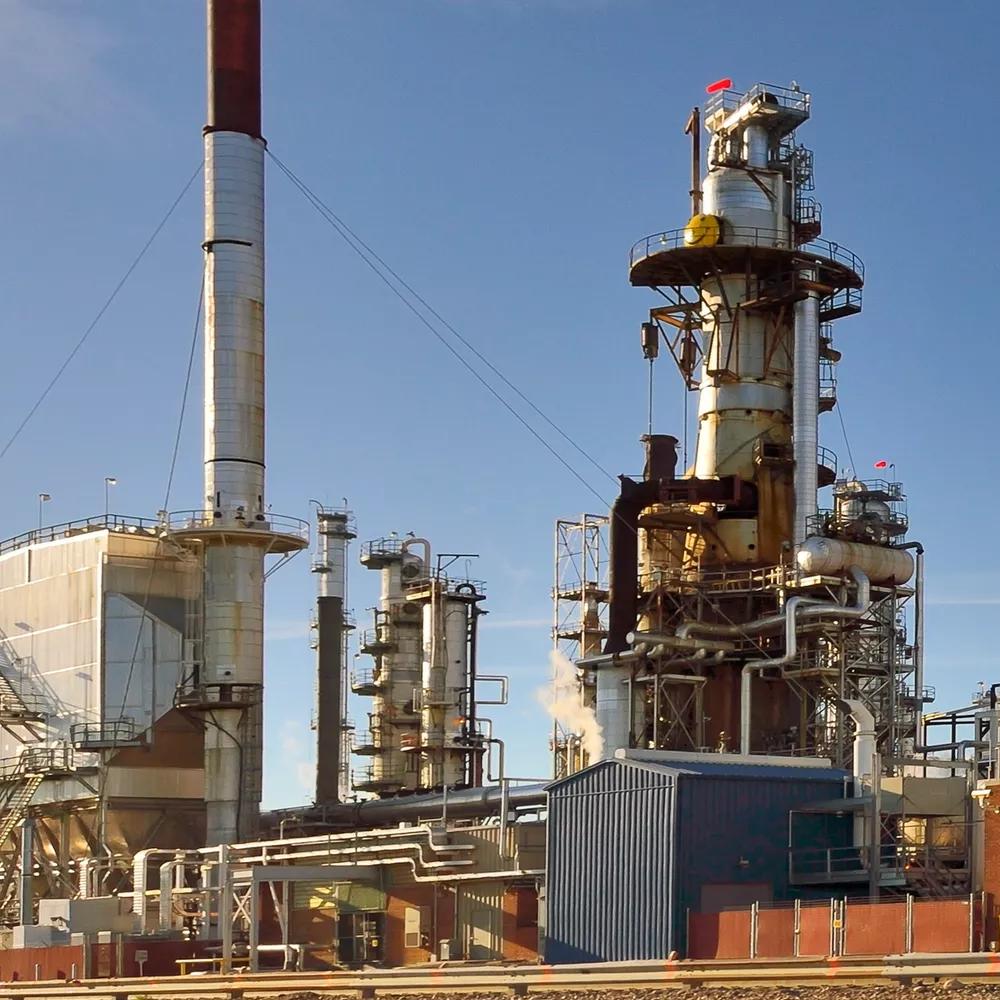 industrial refinery with tall towers, pipes, and structures against a clear blue sky