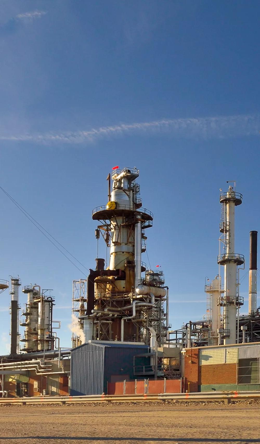 industrial refinery with tall towers, pipes, and structures against a clear blue sky