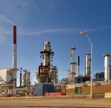 Industrial refinery with tall towers, pipes, and structures against a clear blue sky.