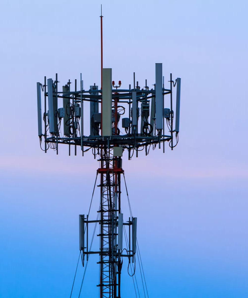 Deux grandes tours de télécommunications avec plusieurs satellites sont représentées devant un ciel vibrant au coucher du soleil.