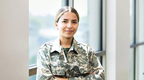 A confident female soldier stands with her arms crossed while working in a recruitment office.