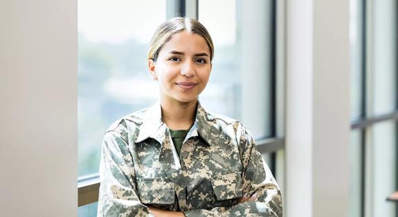 A confident female soldier stands with her arms crossed while working in a recruitment office.